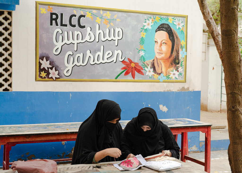 Essere donna in Pakistan - Due donne delle zone rurali del Sindh, emigrate a Karachi con le loro famiglie in cerca di una vita migliore, lavorano alla cucitura di un nuovo prodotto nella sede centrale dell'RLCC. Sullo sfondo, un ritratto dipinto di Rana Liaquat, fondatrice di RLCC nel 1954. RLCC è un'organizzazione non governativa che offre formazione artigianale alle donne delle aree rurali, promuovendo l'indipendenza economica e pratiche eco-sostenibili. Karachi, Pakistan, 15 aprile 2024. <br />
